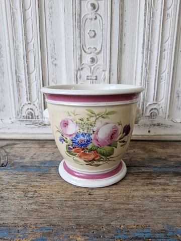 B&G urtepotteskjuler forsynet med hanke i form af kvindeansigter i bisquit. Urtepotten er smukt dekoreret med blomstremotiver 1852-95